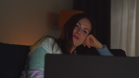 Smiling-Woman-Sitting-On-Sofa-At-Home-At-Night-Streaming-Or-Watching-Movie-Or-Show-On-Laptop-2